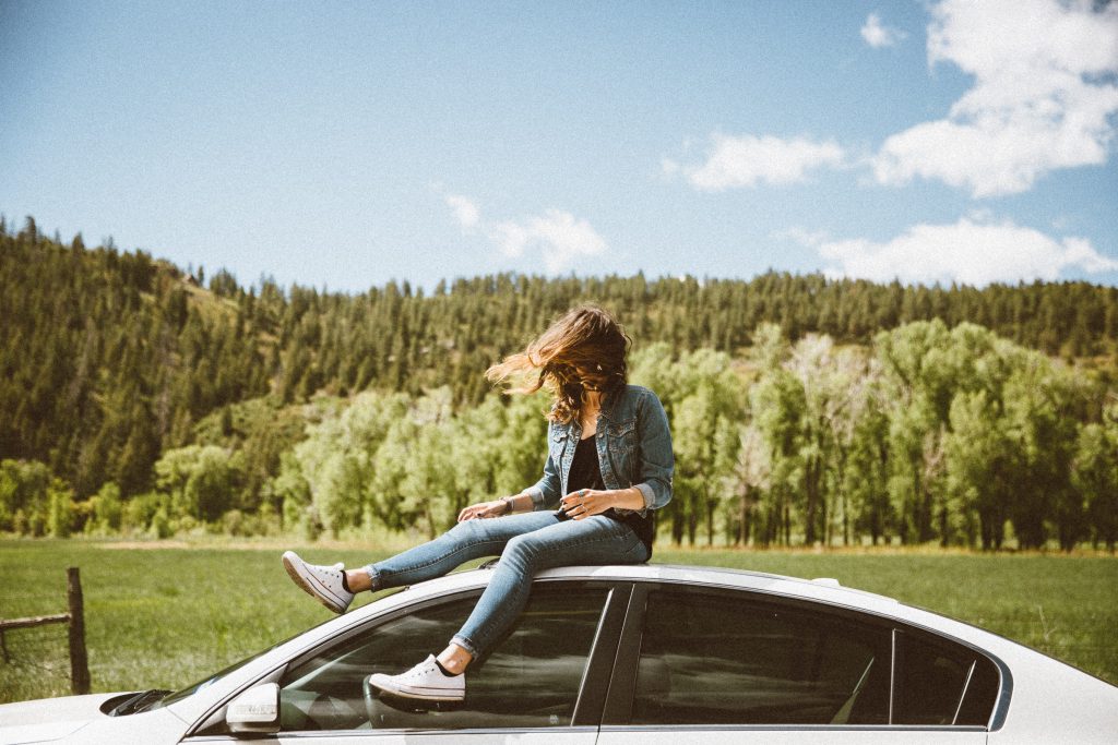 girl on top of car with woods in background